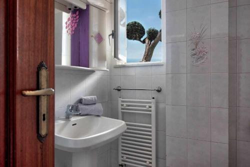 La salle de bains blanche est pourvue d'un lavabo et d'une fenêtre. dans l'établissement Ulivello Country Side Apartment with Sea View, à Massa Lubrense