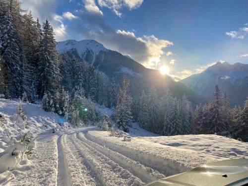 a snow covered road with the sun in the mountains at Haus Schlögl in Pfunds