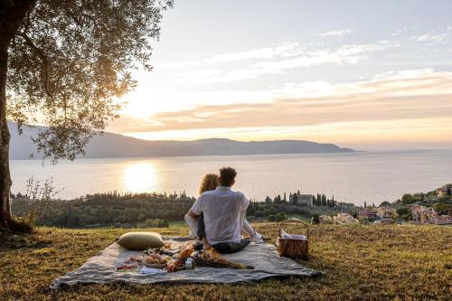 a man and woman sitting on a blanket looking at the water at Colago Private Villas Lake Garda in Toscolano Maderno