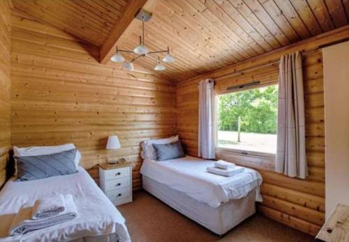 two beds in a log cabin bedroom with a window at Bishops Park Lodges At Fingle Glen Golf Hotel in Exeter