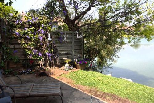 Cosy home in Pecanwood lake view - Hartbeesport في هارتبيسبورت: حديقة فيها كرسي وزهور بجانب الماء