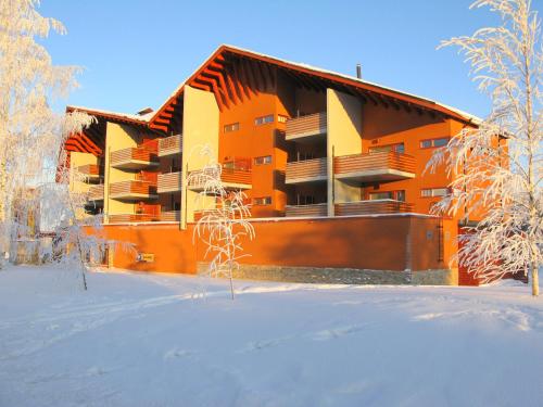 an orange apartment building in the snow with trees at Apartments Tähtitahko in Tahkovuori