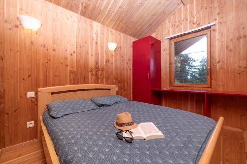 Dormitorio con cama con sombrero y libro en Camping Le Lac des Sapins, en Cublize