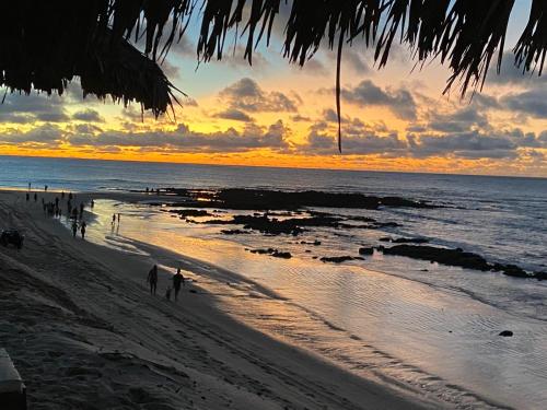 grupa ludzi spacerujących po plaży o zachodzie słońca w obiekcie Flor de Cacto Beach Home w mieście São Miguel do Gostoso