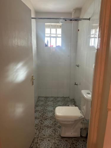 La salle de bains blanche est pourvue de toilettes et d'une fenêtre. dans l'établissement J L appartment, à Eldoret