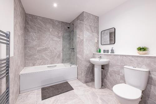 a bathroom with a white tub and a toilet and a sink at Gospel Heights by Guestz in Heswall