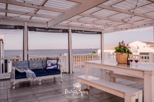 a porch with a bench and a table and the ocean at SHB Sonvanger in St Helena Bay