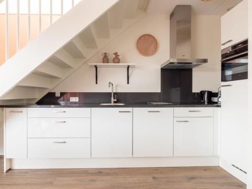 a kitchen with white cabinets and a staircase at Holiday Home De Meerparel by Interhome in Uitgeest