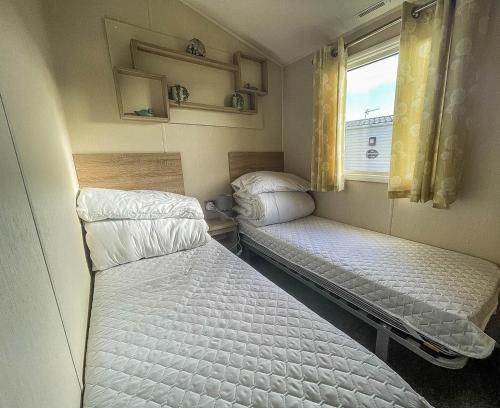two beds in a small room with a window at Spacious Caravan On The Suffolk Coast With Outside Decking Too Ref 20044bs in Hopton on Sea
