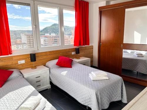 a bedroom with two beds and a window with red curtains at MEQUEDO CALDEREROS 25 in Alcañiz