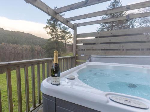 uma garrafa de champanhe sentada numa banheira de hidromassagem num deque em Chalet Lodge 26 by Interhome em Spean Bridge
