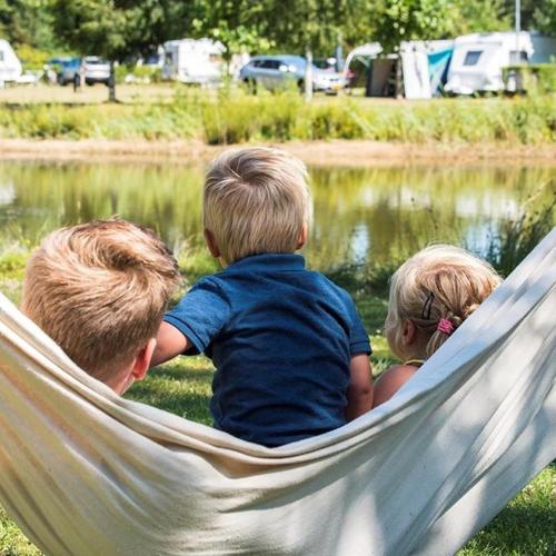 a boy and two children sitting in a hammock near a pond at Camping Heidekamp in Versmold