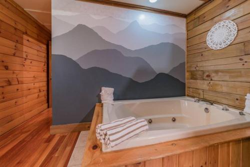 eine Badewanne in einem Zimmer mit einem Wandbild aus den Bergen in der Unterkunft Couples Getaway Cabin near National Park w Hot Tub in Pigeon Forge