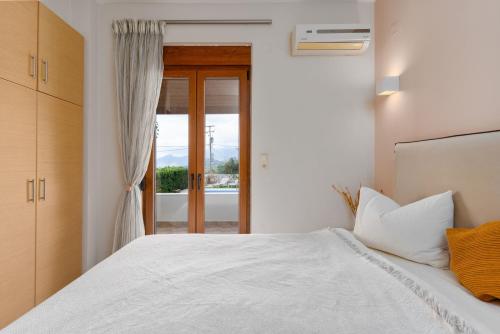 1 dormitorio con cama blanca y puerta de cristal en Myrto Villa with sea view, en Lefkogeia