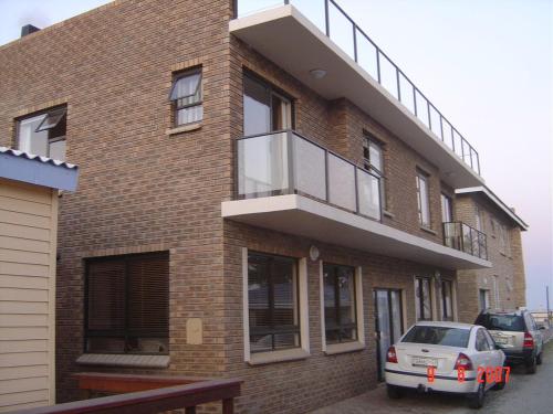 a brick building with a balcony and a car parked outside at Toch Noch in Hartenbos