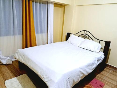 a bedroom with a bed with white sheets and a window at The Carina Homes in Kisumu