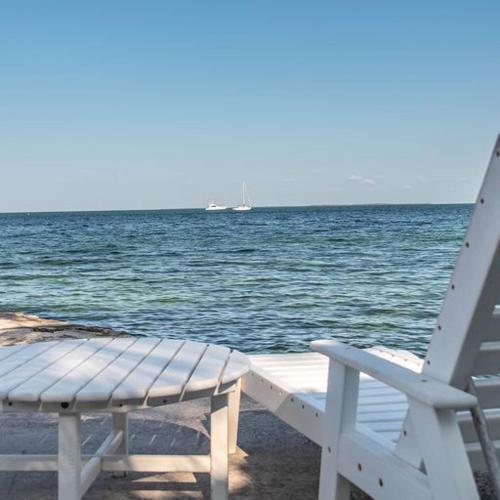 a white chair and a table and a boat in the water at Little Bay Compound in Islamorada