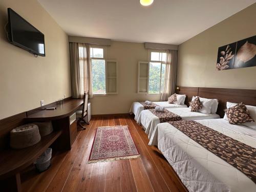 a room with three beds and a desk and a television at Pousada Princesa Isabel - Visconde in Petrópolis