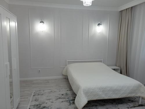 a white bedroom with a bed and two lights on the wall at 1-но комнатная квартира в центре Астаны ЖК Sezim Qala 4 in Astana