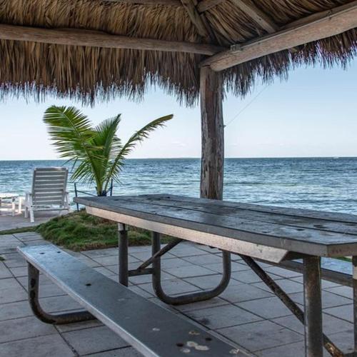 a wooden bench sitting under a straw umbrella on the beach at Little Bay Prime in Islamorada
