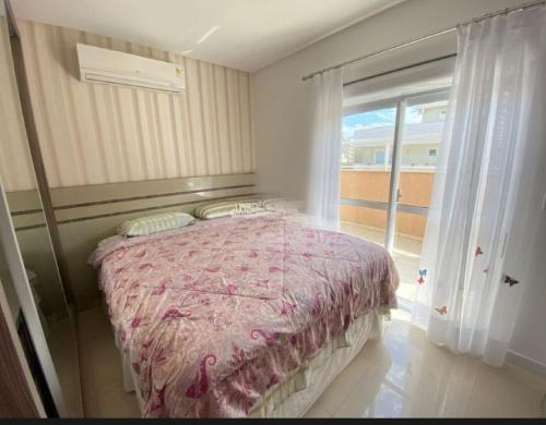 een slaapkamer met een bed en een groot raam bij Suíte em Cobertura, Não é a cobertura toda, somente suíte e piscina in Bombinhas