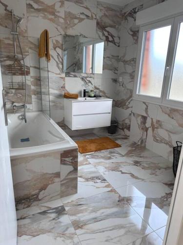 La salle de bains est pourvue d'une baignoire blanche et d'un mur en marbre. dans l'établissement Chez sana, à Saint-Dizier