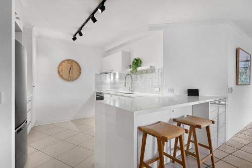 a white kitchen with two bar stools and a sink at Central Location Stylish 3 Bed with Pool - Sunshine Central in Sunshine Beach