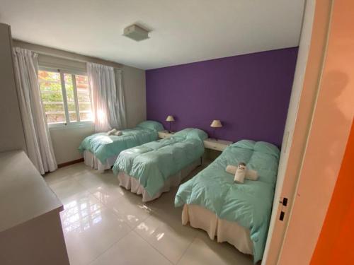 Habitación con 3 camas y pared púrpura. en Cabañas Amalar en Malargüe