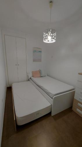 a white bedroom with a bed and a chandelier at Apartamento moderno vacacional in Águilas