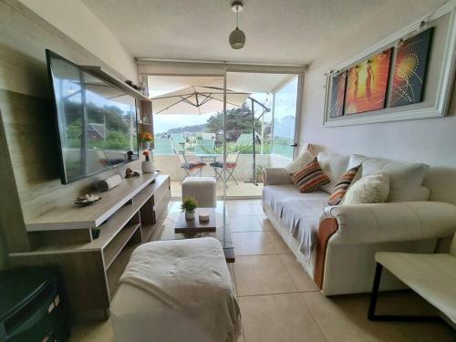 a living room with a couch and a large window at Condominio Miramar El Tabito in El Tabo