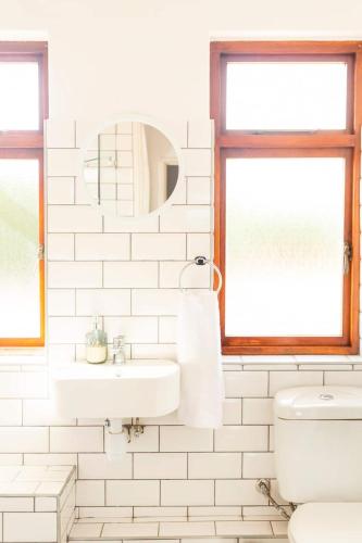 a white bathroom with a sink and a mirror at Innie Baai Beach House in Cape Town