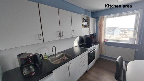 una cucina con armadi bianchi, lavandino e finestra di Ilulissat Apartment a Ilulissat