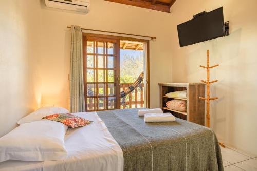 a bedroom with a bed with a tv and a window at Pousada do Paraiso in Barra de Ibiraquera