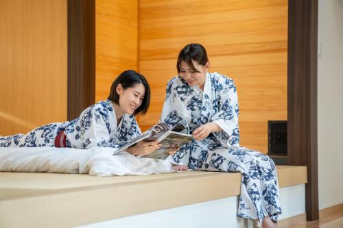 dos mujeres sentadas en una cama leyendo un libro en Villa Miyako 源泉かけ流し客室温泉ヴィラ みやこ別邸 en Goto
