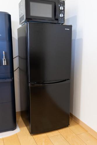 a black refrigerator with a microwave on top of it at 丘の上から海が見える一棟貸しヴィラ しまいろ長手 in Nagate