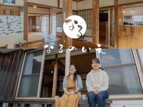 two people sitting on the front of a house at なるのいえ 港から徒歩1分 サウナと広々リビングの宿byしまいろ in Ura