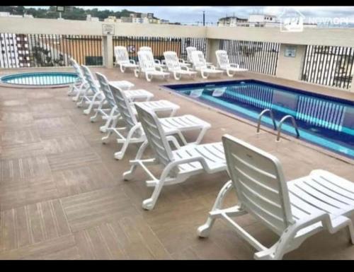 a row of white lounge chairs next to a swimming pool at Apartamento Flat Palladium in São Vicente