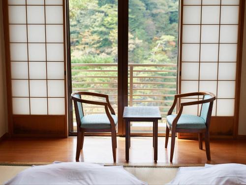 two chairs and a table in front of a window at Tabist Nikkokinugawa Onsen Kiyomizu no Yado in Nikko