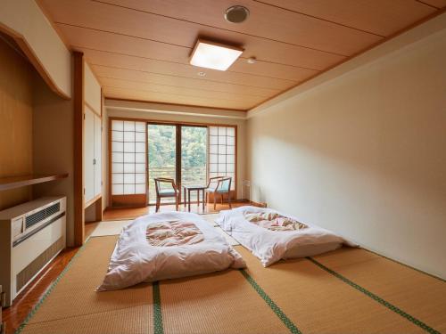 two beds in a room with a table and chairs at Tabist Nikkokinugawa Onsen Kiyomizu no Yado in Nikko