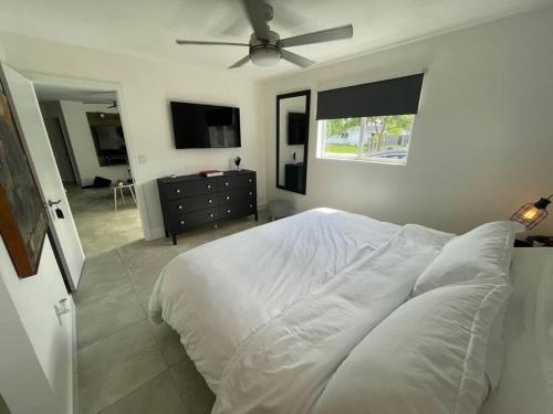 a bedroom with a white bed with a ceiling fan at Modern pool home on the lake near Hardrock FLL airport in Davie