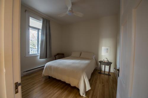 a white bedroom with a bed and a window at Pignon sur Parc in Trois-Rivières