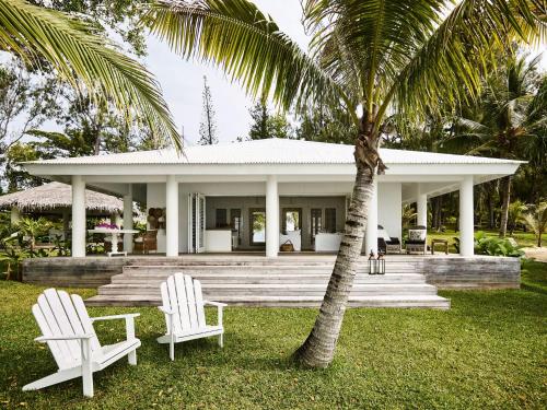 two white chairs and a house with a palm tree at Tamarind Beach Estate in Port Vila