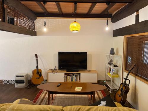a living room with a tv and a table and guitars at 和良ポポハウス in Gujo