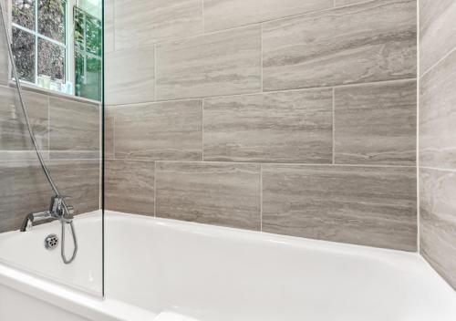a bathroom with a white bath tub and a tile wall at Radiant Serenity: 2BR Flat Sleeps 5 -Warm Ambiance in London