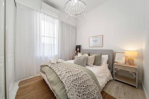 a white bedroom with a bed and a chandelier at Marseille Glenelg - Firepit BBQ Central in Glenelg