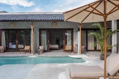 a swimming pool with an umbrella next to a house at Kano Twin in Canggu
