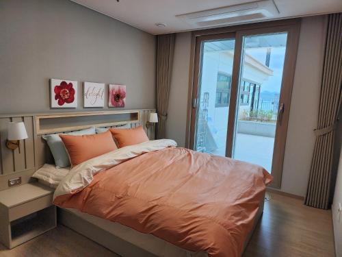 a bedroom with a bed with an orange comforter and a balcony at Ungcheon Hotel Travel Bag in Yeosu