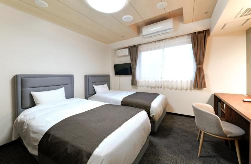 a hotel room with two beds and a desk and a window at 朝里川温泉ホテル in Otaru