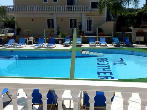 a large swimming pool with blue chairs and a house at Two Brothers Studios Tsilivi Zakynthos in Tsilivi