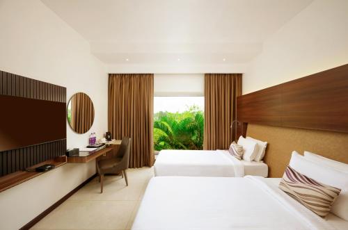 a hotel room with two beds and a desk at Flora Airport Hotel and Convention Centre Kochi in Nedumbassery